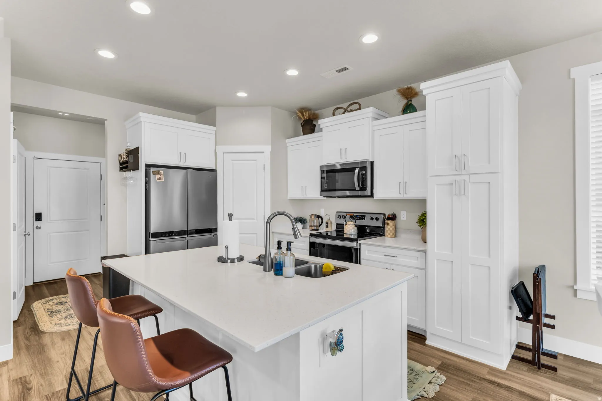 Kitchen featuring white shaker-style cabinetry, stainless steel appliances, a center island with sink, quartz countertops, and recessed lighting