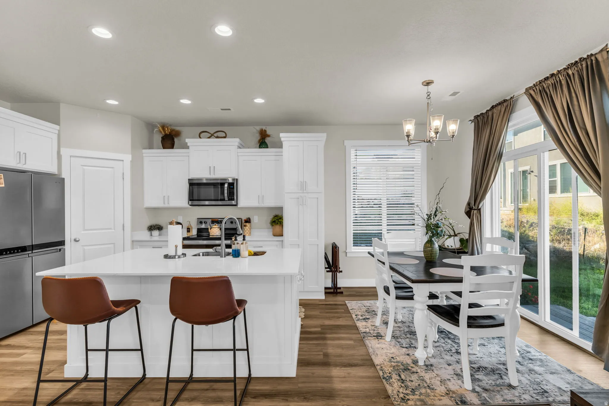 Open-concept living space with wood-finish flooring, white cabinetry, a kitchen island with seating, a dining area, and sliding glass doors
