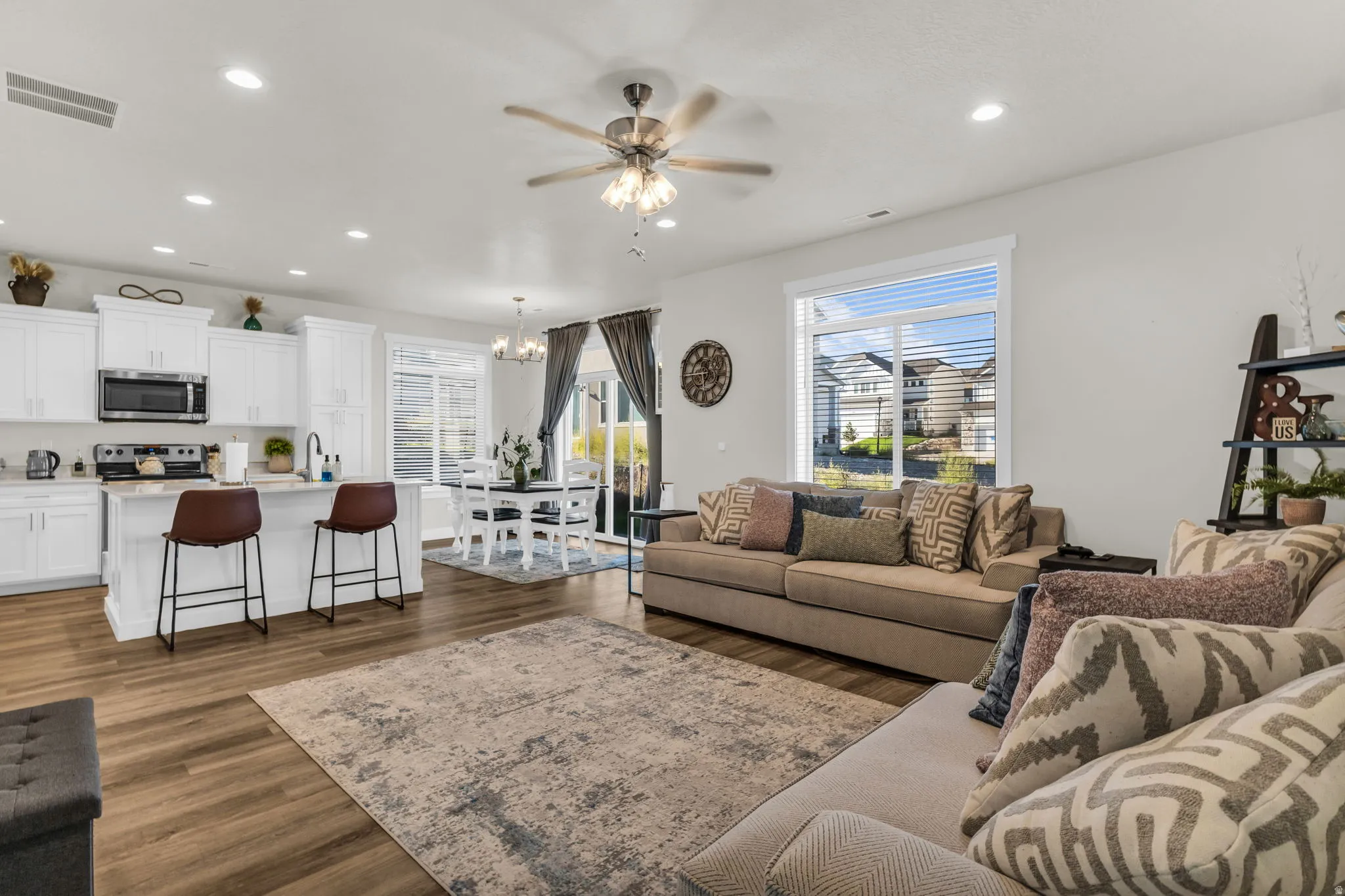 Open-concept living area featuring wood-finish flooring, white cabinetry, a kitchen island with seating, a dining area, and a ceiling fan
