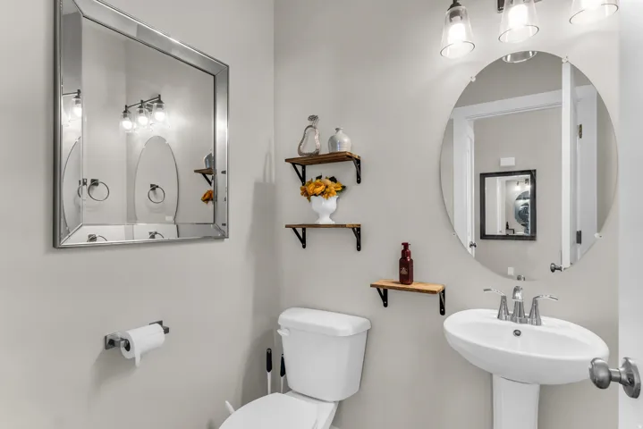 Pedestal sink with chrome faucet, wall-mounted light fixture, and square mirror with a beveled frame