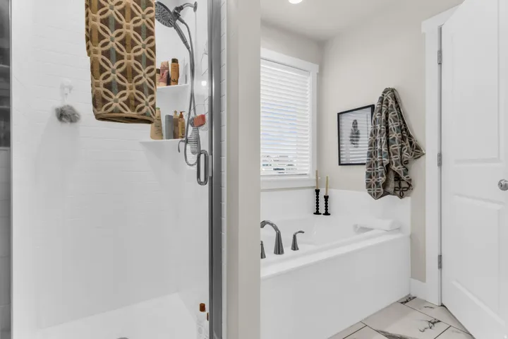 Built-in soaking tub with deck-mounted faucet, shower with white subway tile surround, clear glass shower enclosure, and light-toned flooring