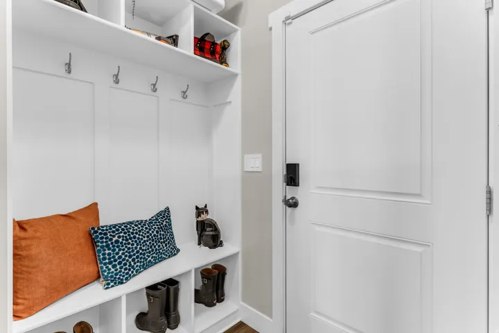 Built-in white storage bench with integrated shelving, multiple coat hooks, and paneled backing