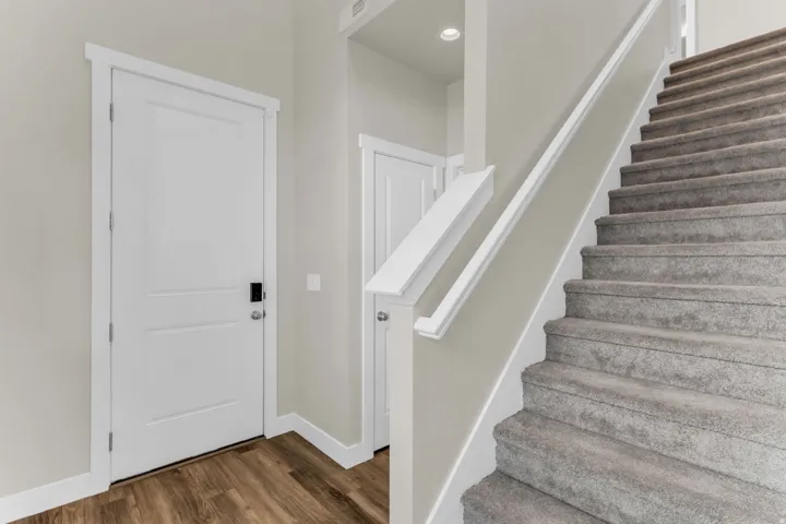 Wood-finish flooring, white paneled doors, carpeted staircase, white railing, recessed lighting
