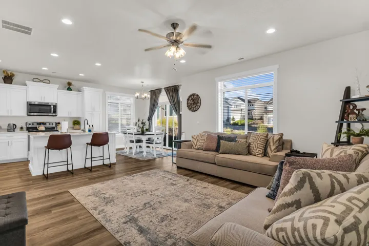 Open-concept living area featuring wood-finish flooring, white cabinetry, a kitchen island with seating, a dining area, and a ceiling fan