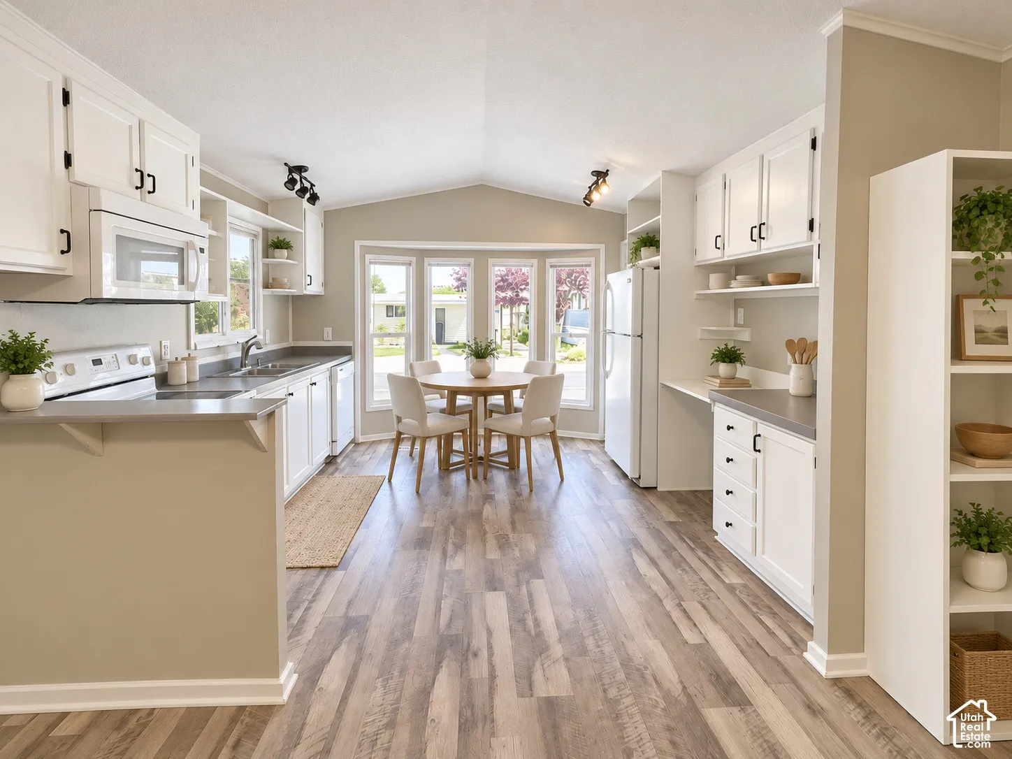 Spacious kitchen featuring wood-finish flooring, white cabinetry, dark countertops, a built-in microwave, and an integrated dining area with bay windows