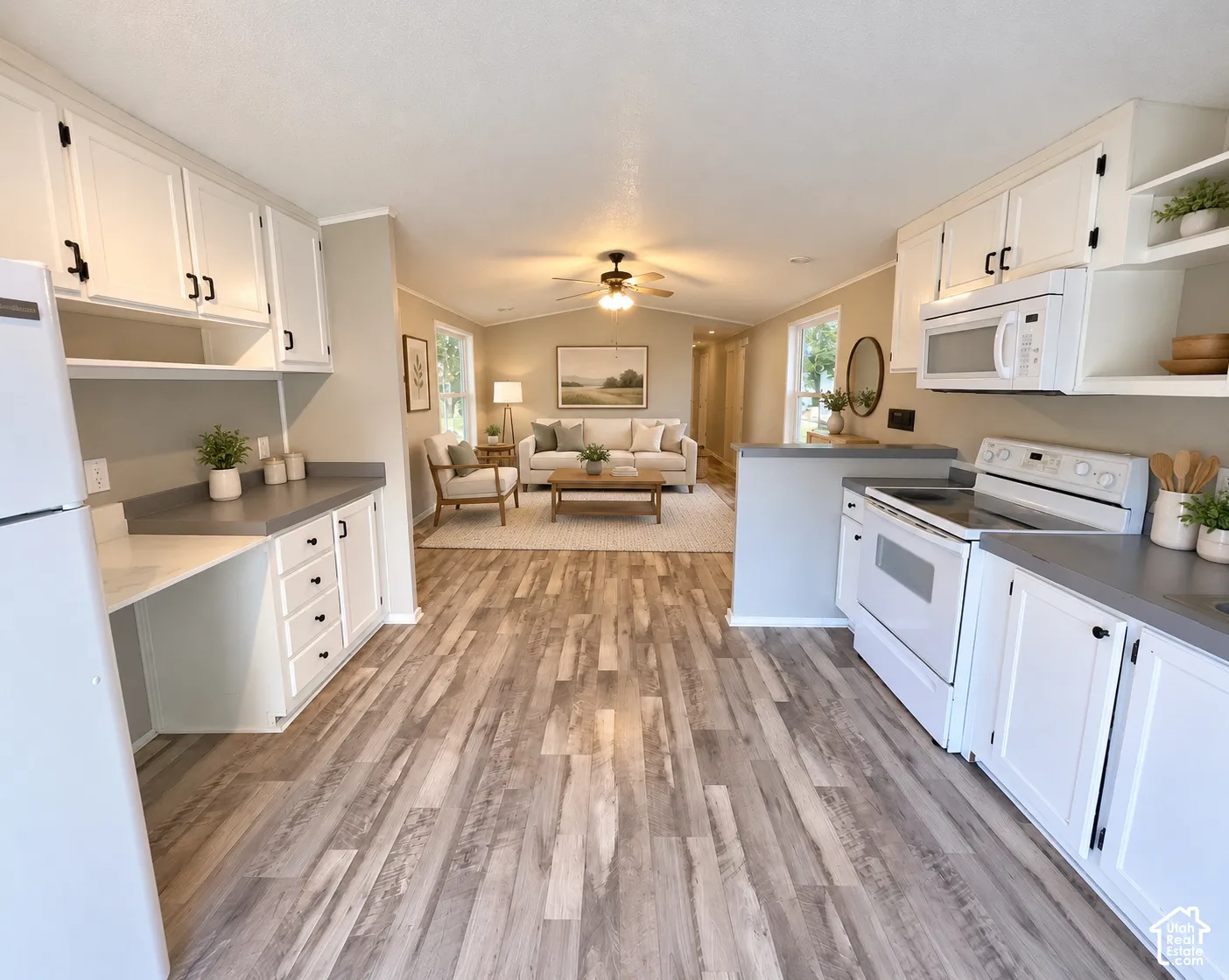 Wood-finish flooring, white cabinetry with black hardware, built-in desk area, white appliances, and a ceiling fan