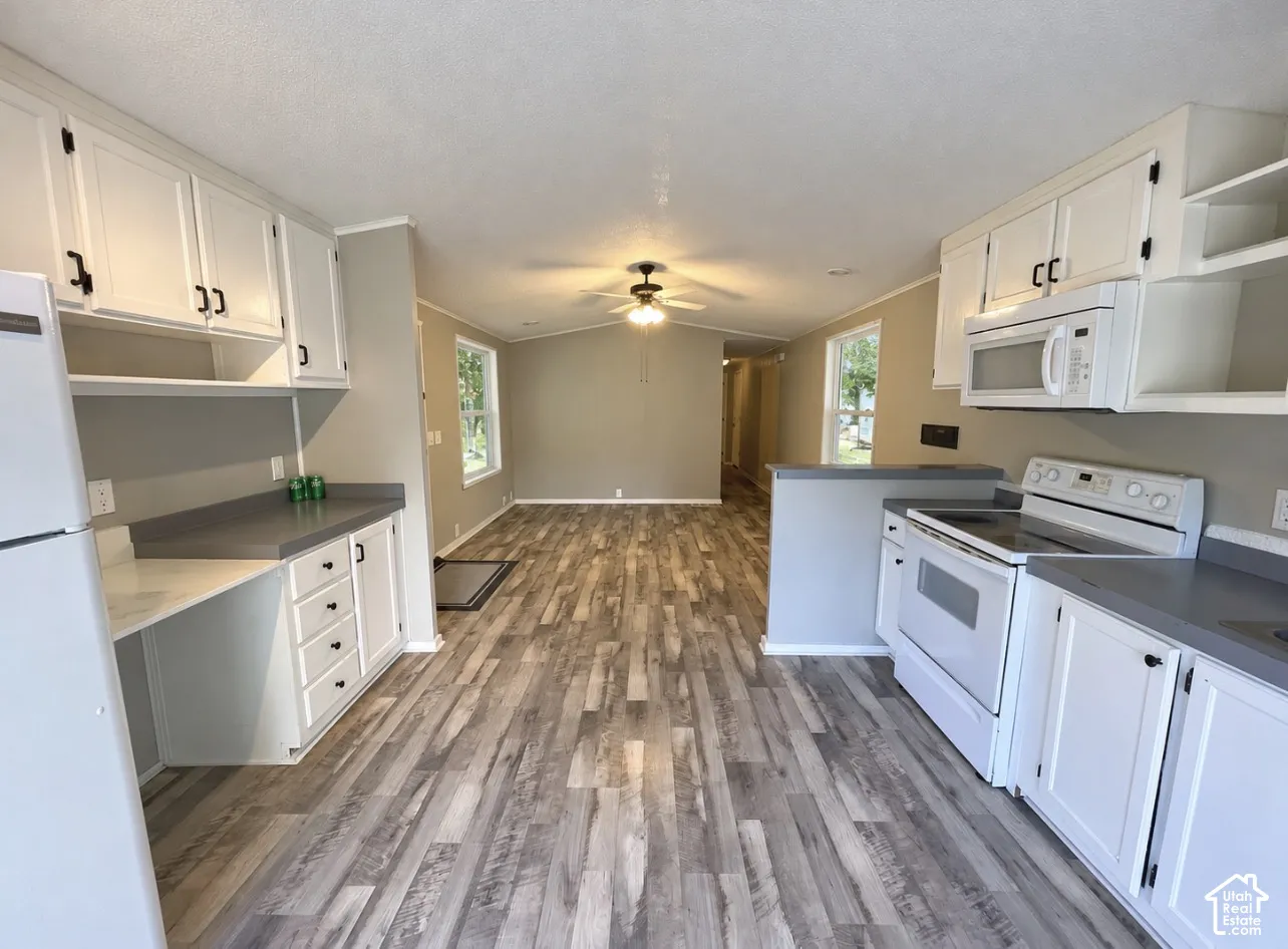 Kitchen featuring white cabinetry, gray countertops, white appliances, and wood-finish flooring