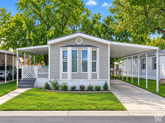 Siding exterior with multiple windows, covered front entrance, carport structure, concrete driveway, and landscaped front yard