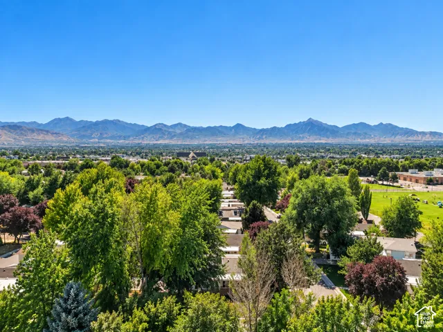 Expansive urban landscape with extensive tree cover, distant mountain range, residential rooftops, and green recreational areas