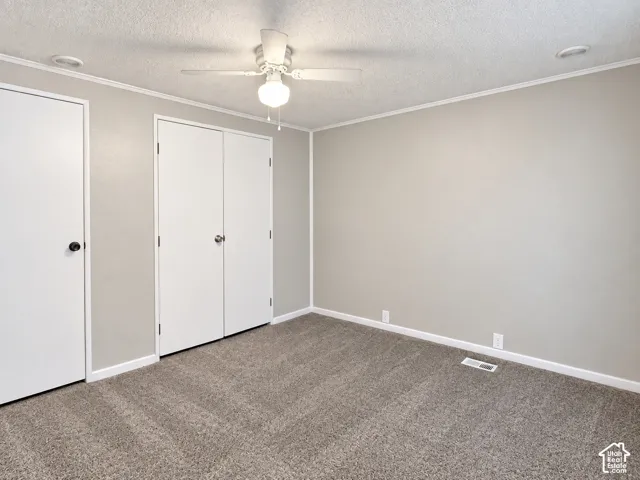 Neutral-toned walls with white trim, gray carpet, white bi-fold closet doors, and a ceiling fan with integrated lighting