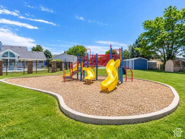 Outdoor play structure with multiple slides and climbing elements, set on a wood chip surface, bordered by a concrete curb and expansive green lawn