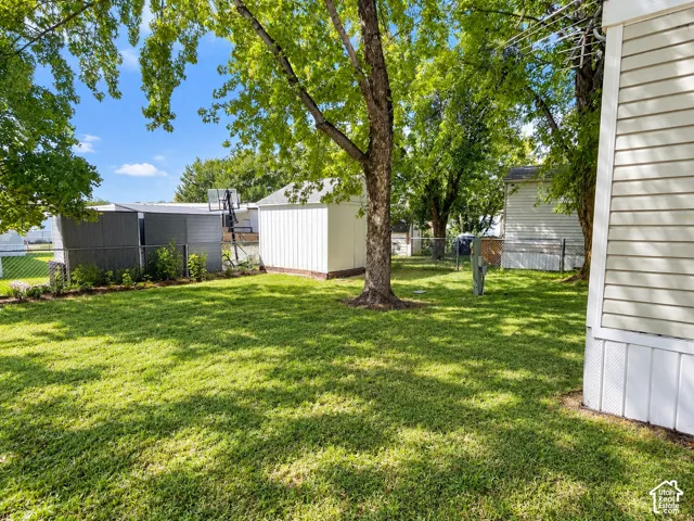 Expansive green lawn, mature shade trees, white-sided outbuilding, and chain link fencing