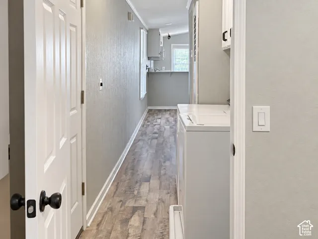 Hallway with wood-finish flooring, light gray wall paint, white trim, and white paneled doors with black hardware