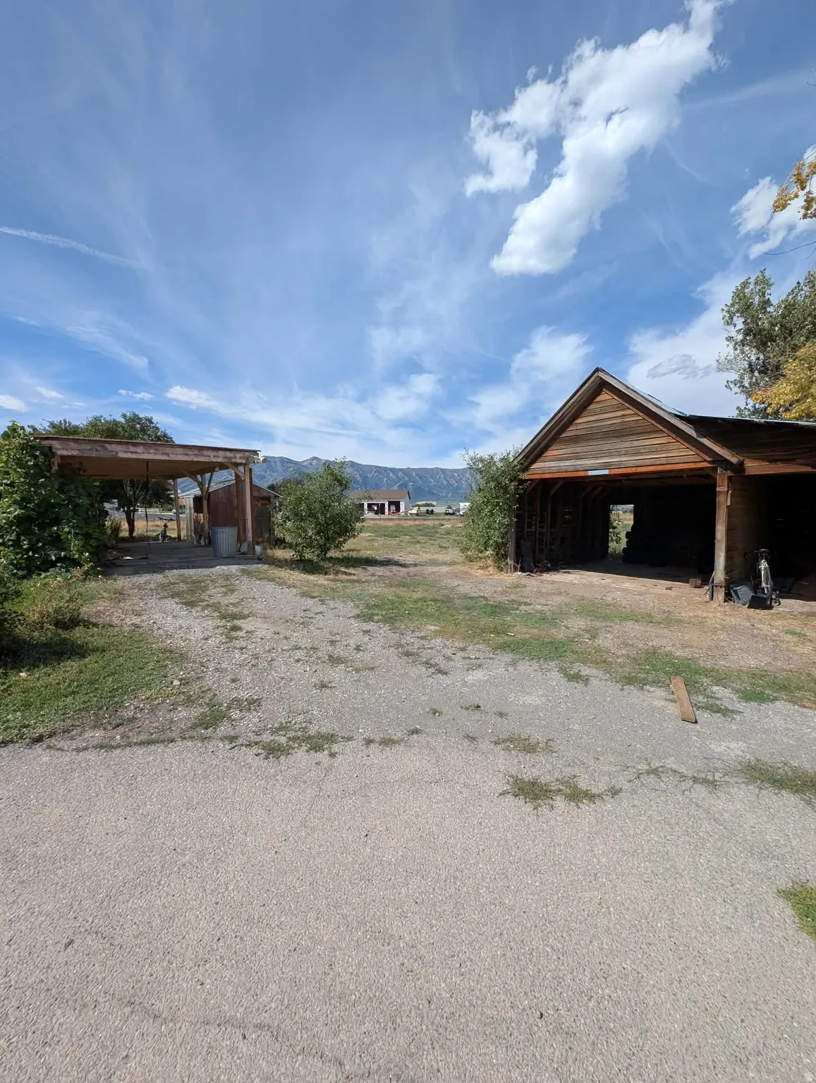 Expansive gravel area with a covered carport and an open-sided outbuilding