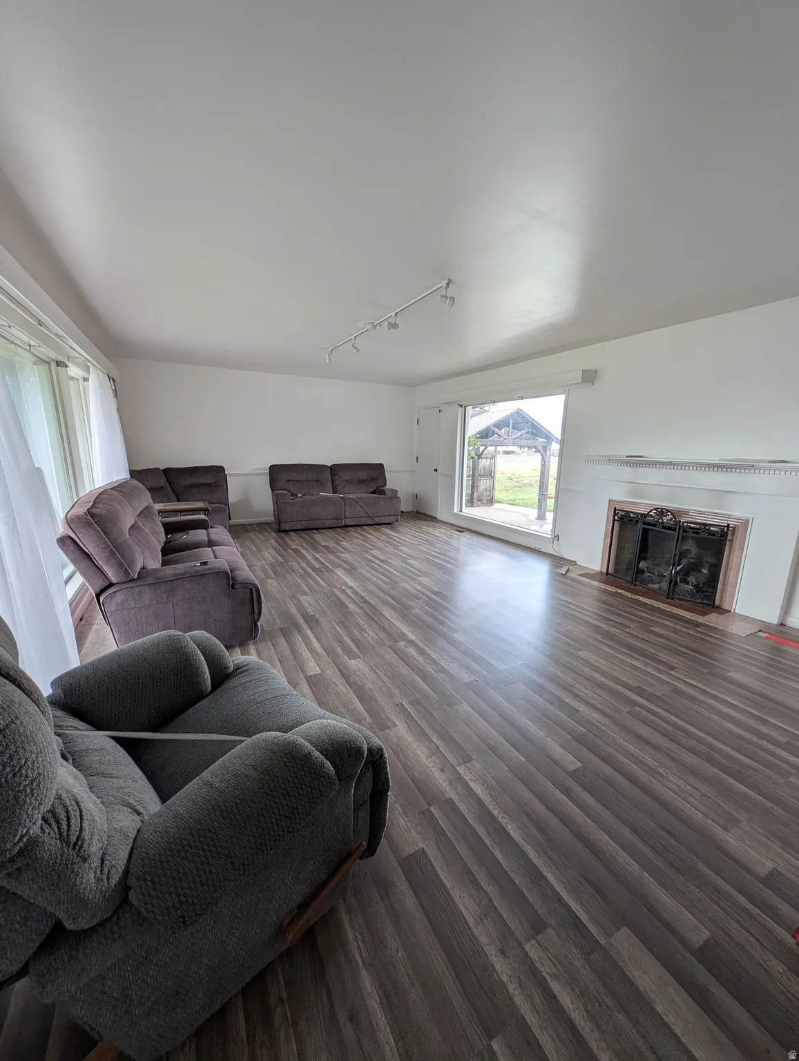 Spacious living area featuring wood-finish flooring, track lighting, and a fireplace with a decorative mantel and hearth