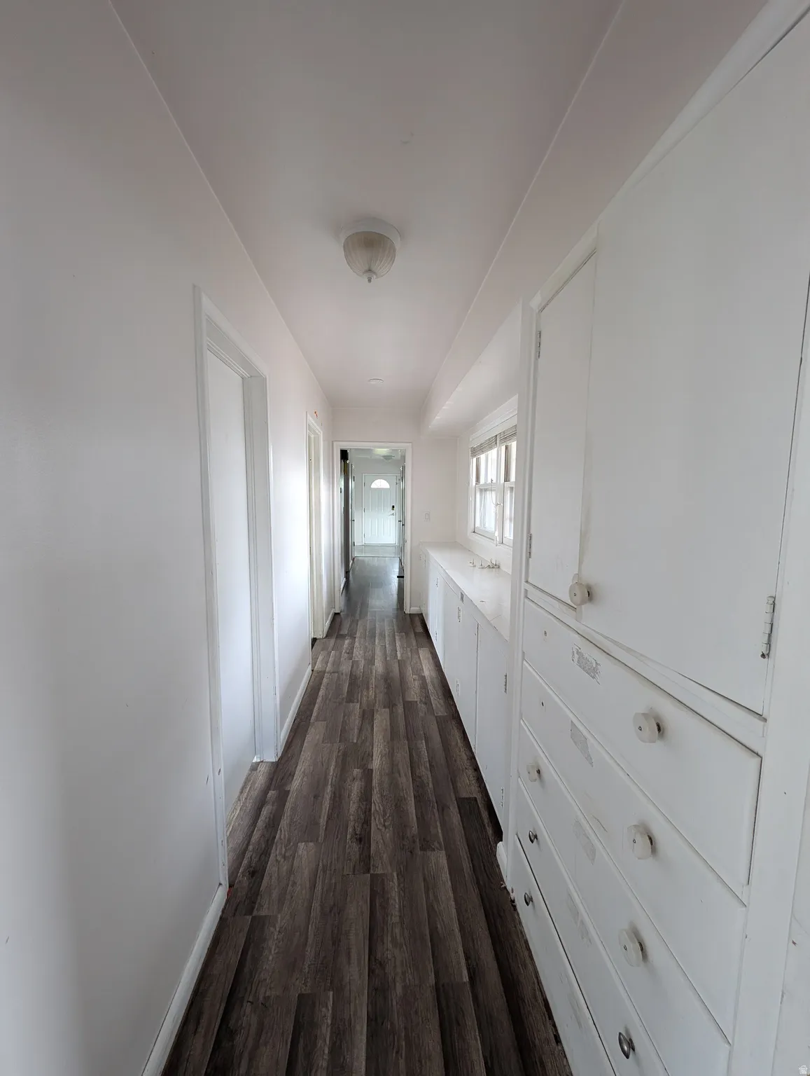 Wood-finish flooring throughout, bright white walls, recessed ceiling fixture, and built-in cabinetry with drawers and storage units