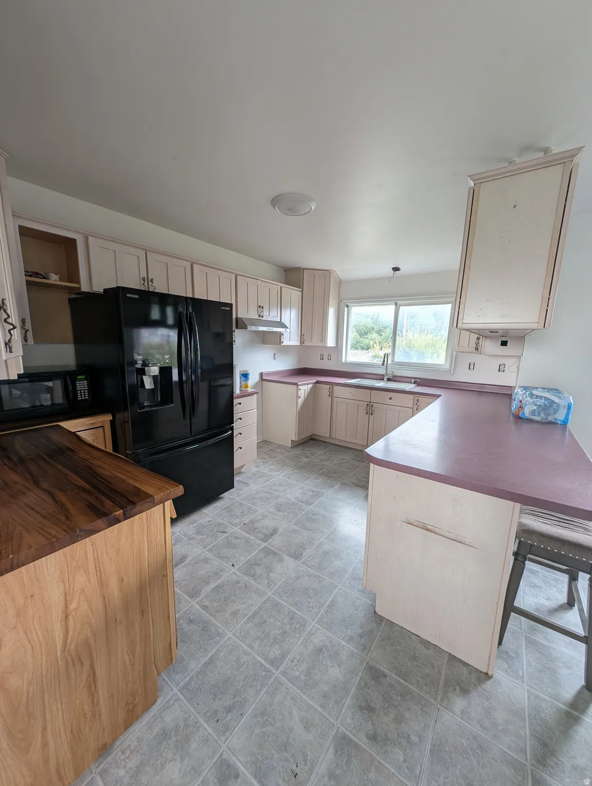 Kitchen featuring extensive cabinetry, L-shaped counter space, a built-in kitchen island with wood-finish countertop, and a window above the sink