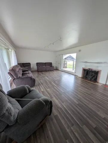 Spacious living area featuring wood-finish flooring, track lighting, and a fireplace with a decorative mantel and hearth