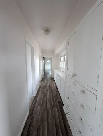 Wood-finish flooring throughout, bright white walls, recessed ceiling fixture, and built-in cabinetry with drawers and storage units