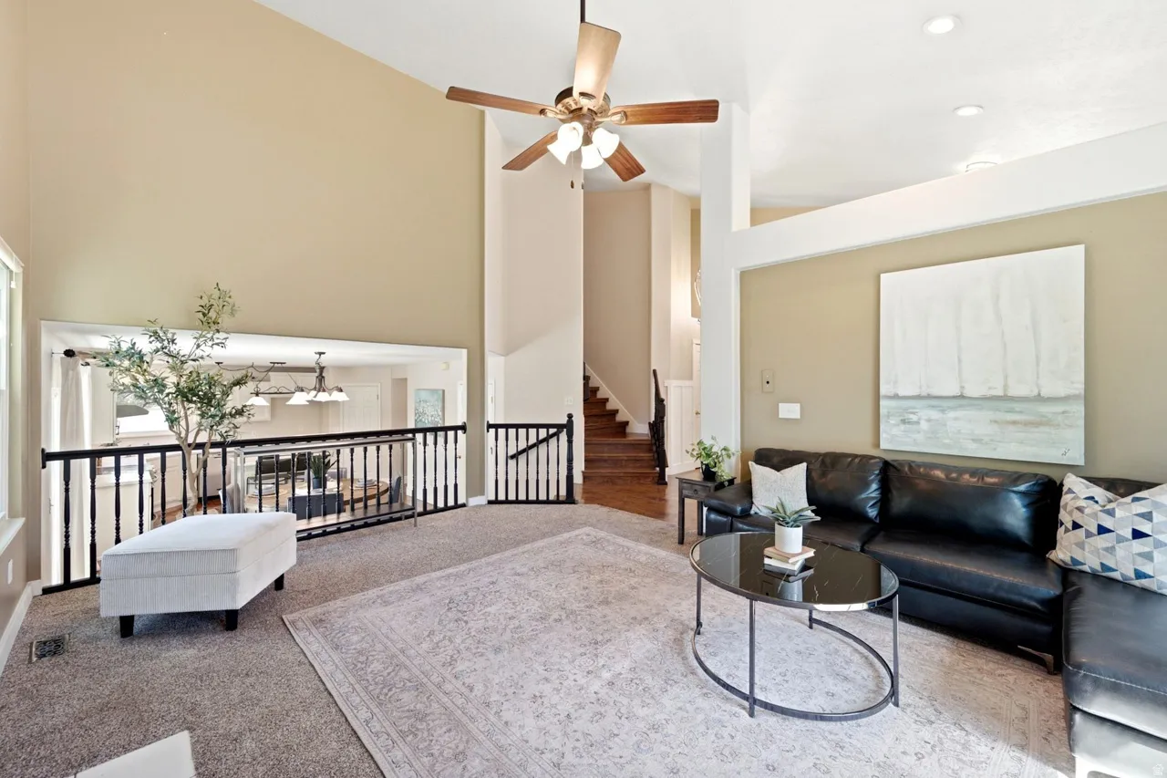 Vaulted ceiling with a ceiling fan, carpeted flooring, black metal railing, and a staircase with wood-finish treads