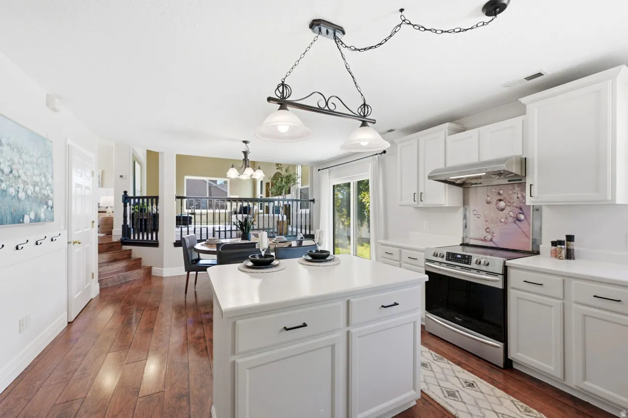 Hardwood flooring, white cabinetry, stainless steel appliances, white countertops, and a kitchen island