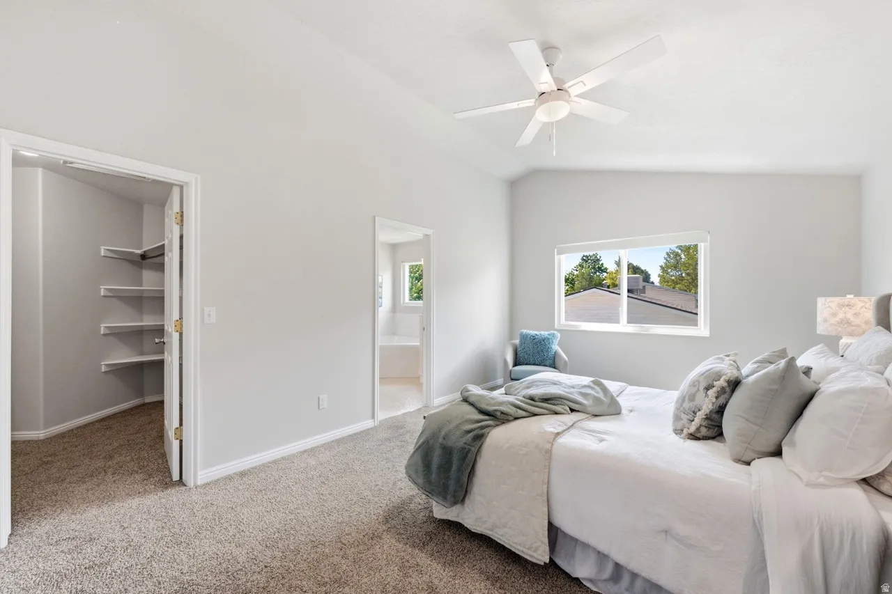 Vaulted ceiling with a contemporary ceiling fan, window with roller shade, carpeted flooring, and built-in closet shelving