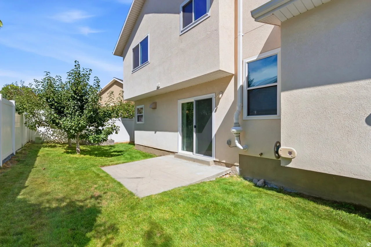 Private fenced backyard with mature trees, concrete patio, and sliding glass door access