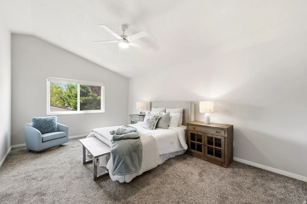 Vaulted ceiling with a ceiling fan, window with roller shade, and plush carpeting
