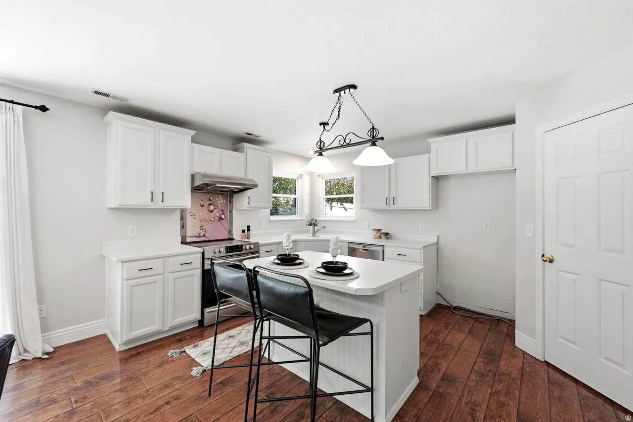White cabinetry with dark hardware, wood-finish flooring, stainless steel range and hood, white countertops, and a central island with seating