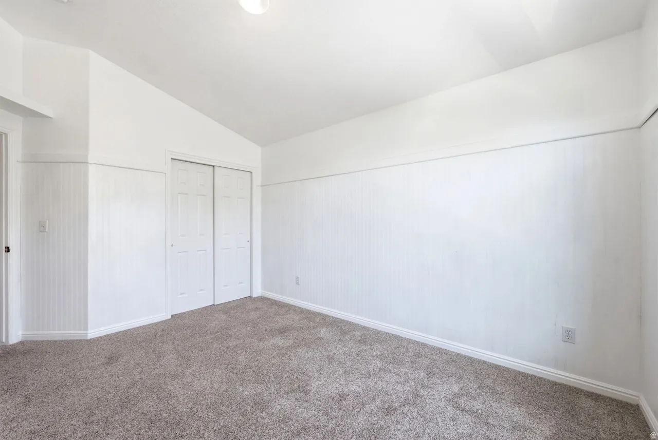 Vaulted ceiling with an overhead light fixture, textured wall panels, neutral-toned carpeting, and a bi-fold closet door