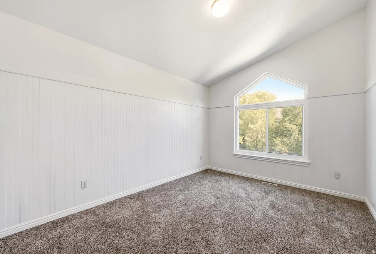 Vaulted ceiling room with an arched window, white paneled lower walls, and dark gray carpeting
