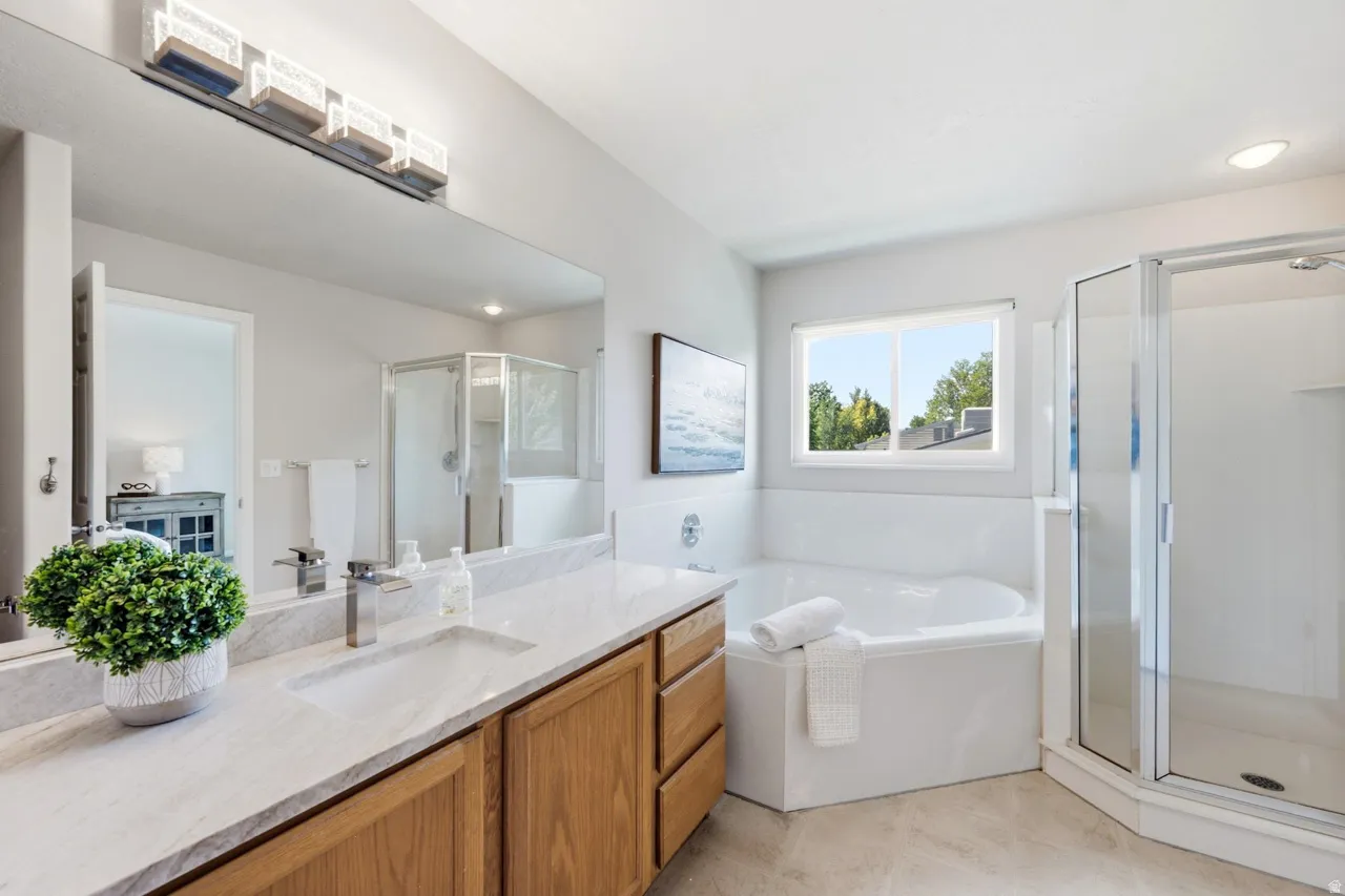 Spacious bathroom featuring a built-in soaking tub, glass-enclosed shower, large vanity with light-tone wood cabinetry, and a light-toned countertop with integrated sink