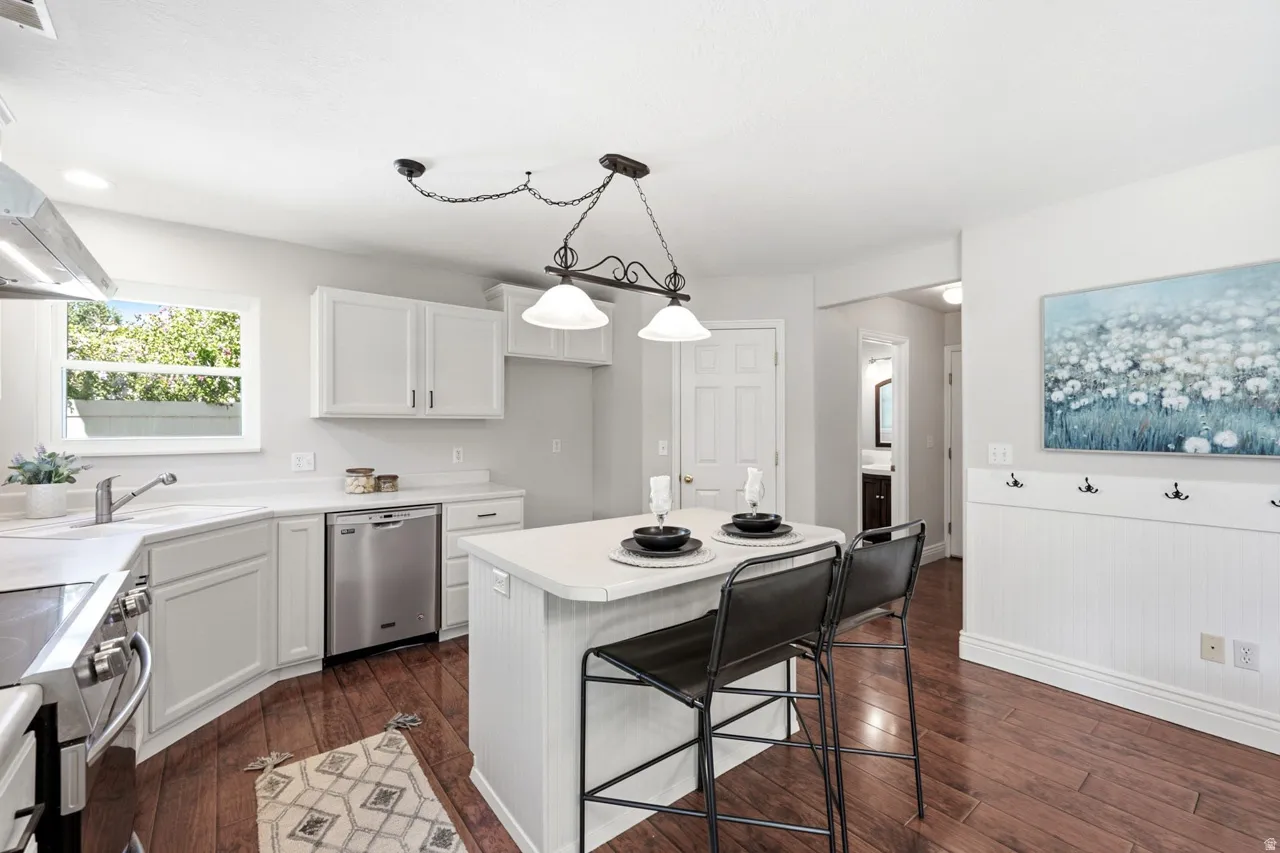 Kitchen featuring a central island, white cabinetry, stainless steel appliances, wood-finish flooring, and a window with natural light
