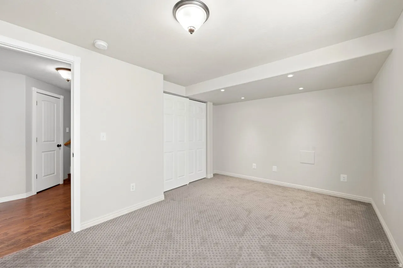 Wall-to-wall patterned carpet, recessed ceiling lighting, overhead ceiling fixture, white bi-fold closet doors, and wood-finish flooring in the adjacent hallway