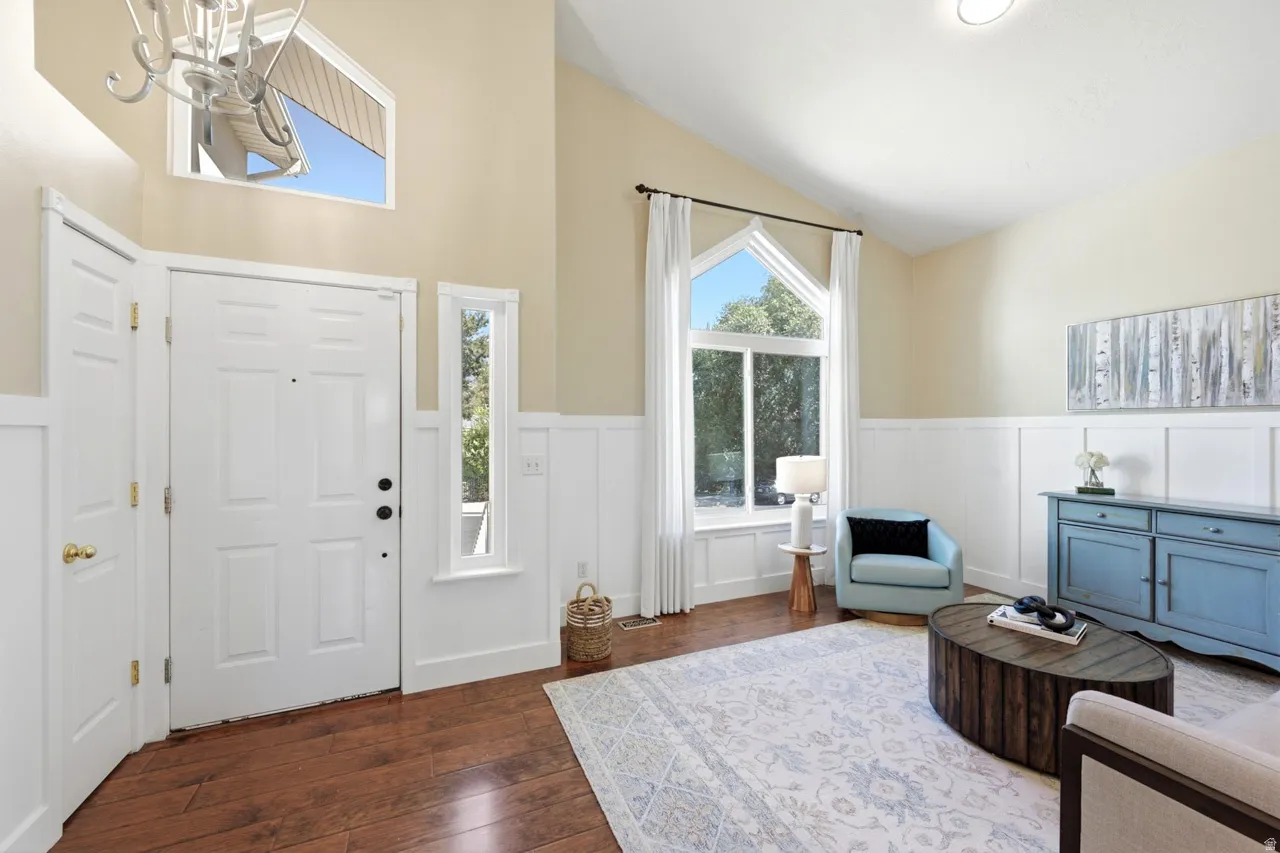 Vaulted ceilings with a decorative light fixture, wood-finish flooring, and white wainscoting