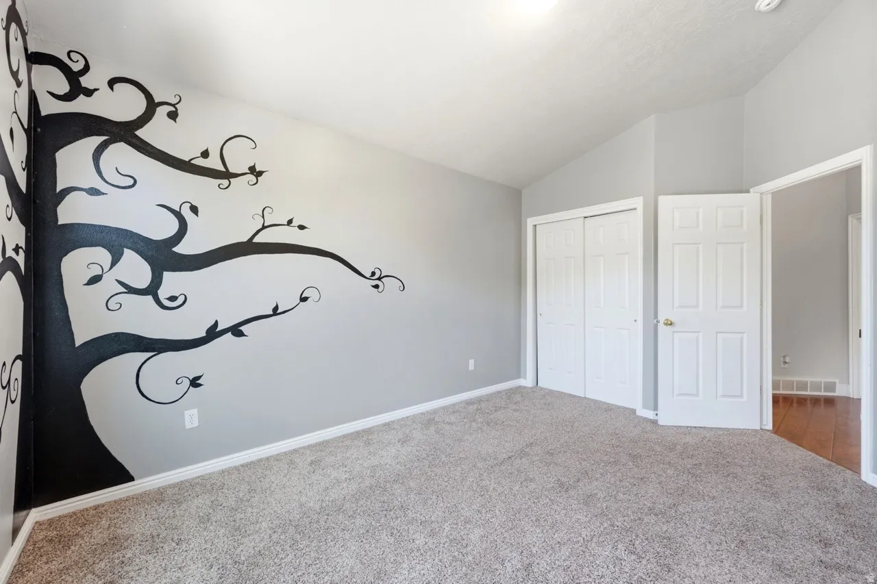 Carpeted flooring, vaulted ceiling, built-in closet with sliding doors, white trim, and a decorative wall graphic