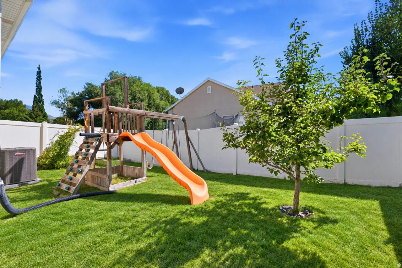 Expansive backyard featuring a manicured lawn, white vinyl fencing, and a young deciduous tree