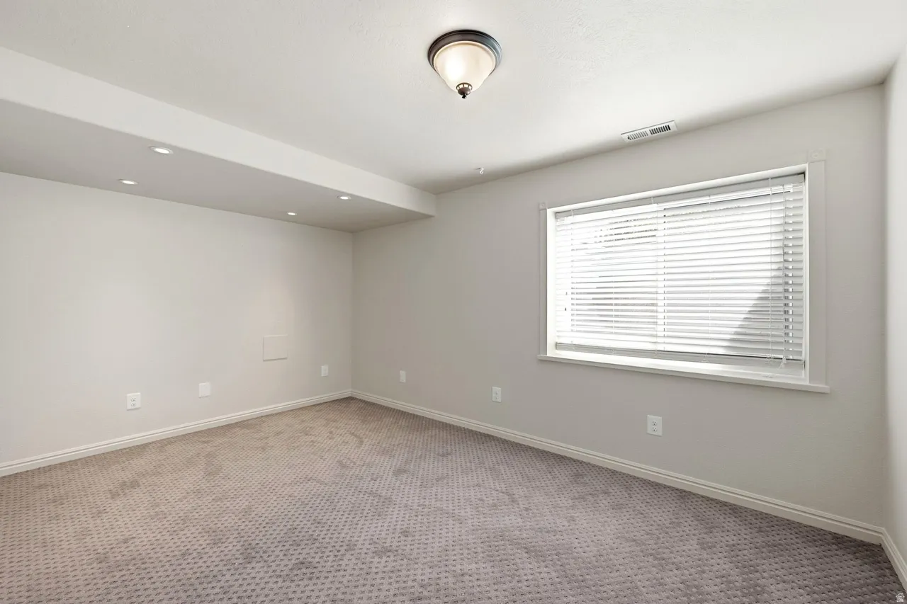 Neutral wall paint, recessed lighting, ceiling-mounted light fixture, window with blinds, and patterned carpeting