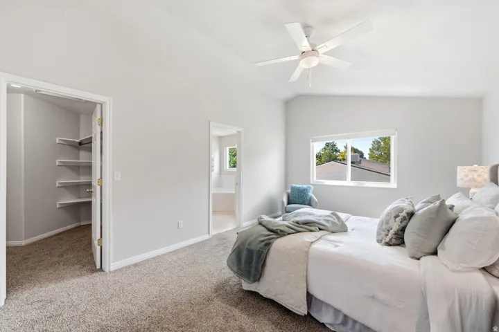 Vaulted ceiling with a contemporary ceiling fan, window with roller shade, carpeted flooring, and built-in closet shelving