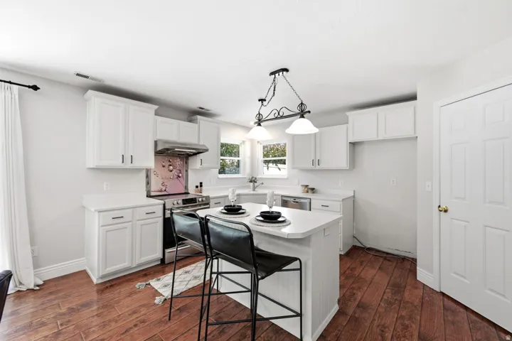 White cabinetry with dark hardware, wood-finish flooring, stainless steel range and hood, white countertops, and a central island with seating