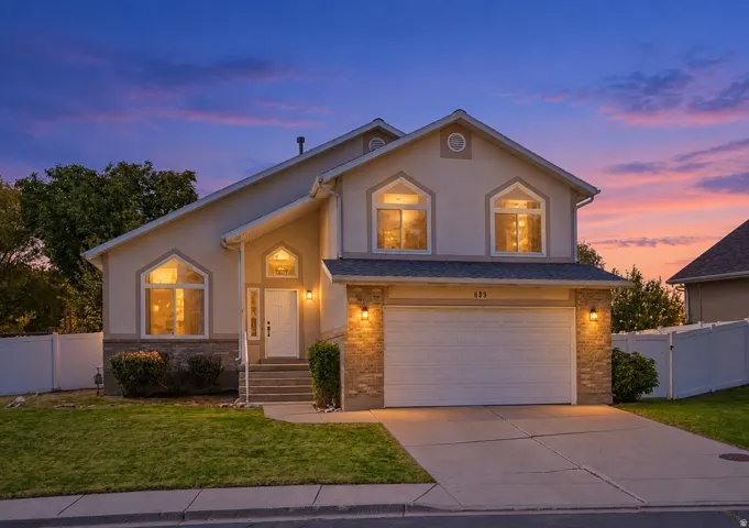 AI enhanced twilight.  Stucco exterior with stone accent, arched window details, attached garage, concrete driveway, and front entry with steps