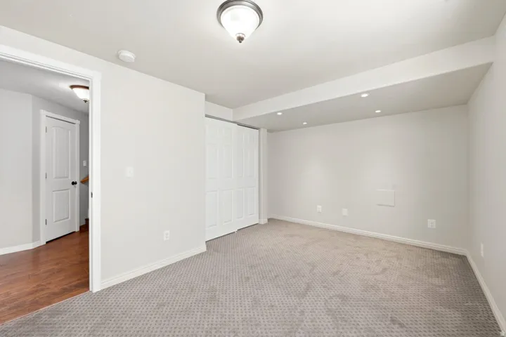 Wall-to-wall patterned carpet, recessed ceiling lighting, overhead ceiling fixture, white bi-fold closet doors, and wood-finish flooring in the adjacent hallway