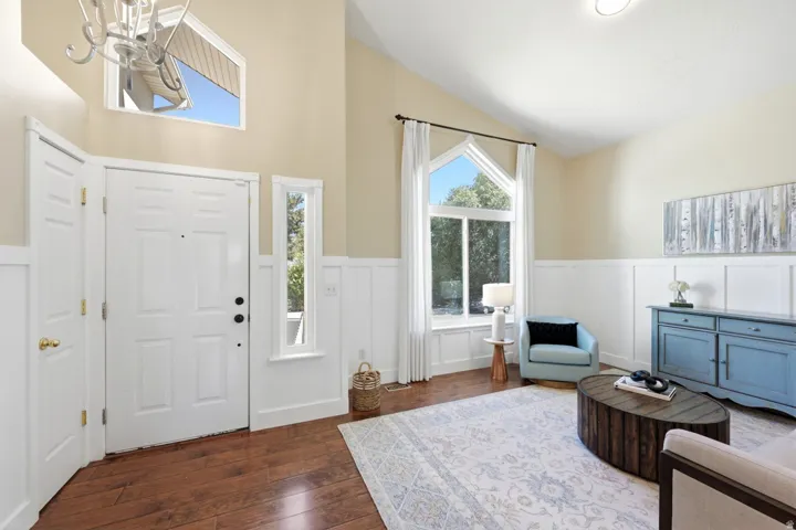 Vaulted ceilings with a decorative light fixture, wood-finish flooring, and white wainscoting