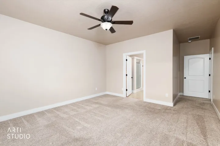 Neutral tone wall paint, textured carpet flooring, ceiling fan with integrated lighting, and white interior doors