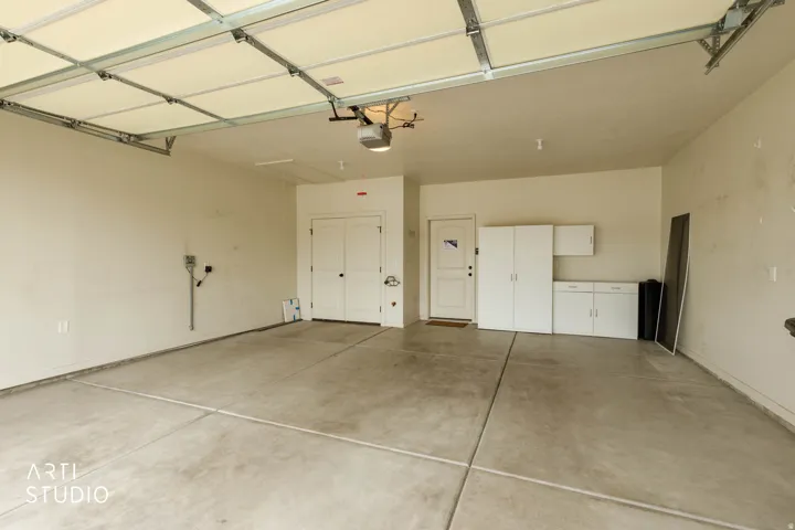 Concrete flooring, overhead garage door system, white cabinet storage, double white panel doors, and a single white panel door