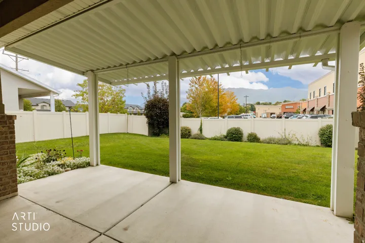 Covered concrete patio with a corrugated ceiling, brick pillar accents, a manicured lawn, and perimeter fencing