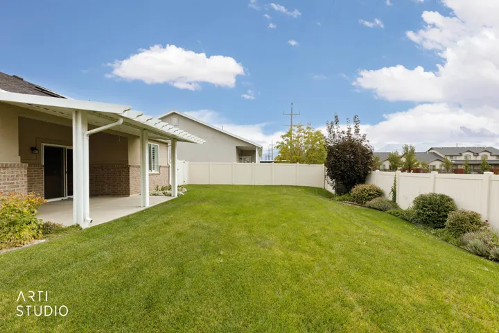 Expansive backyard featuring a manicured lawn, white vinyl fencing, and mature landscaping