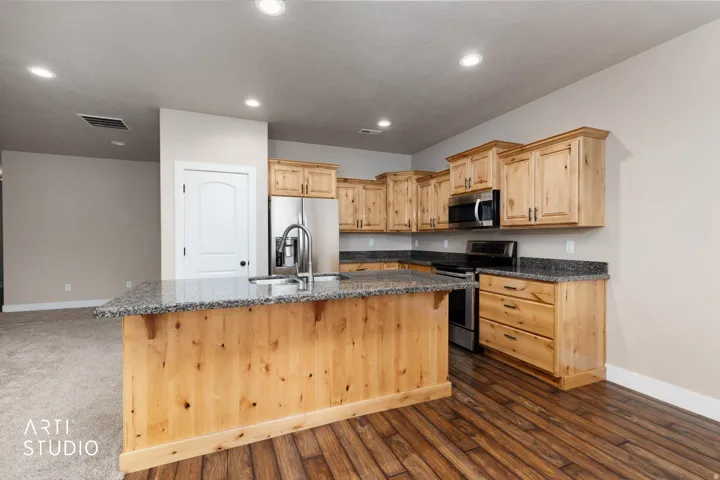 Kitchen featuring wood-finish cabinetry, granite countertops, stainless steel appliances, and a central island with an undermount sink