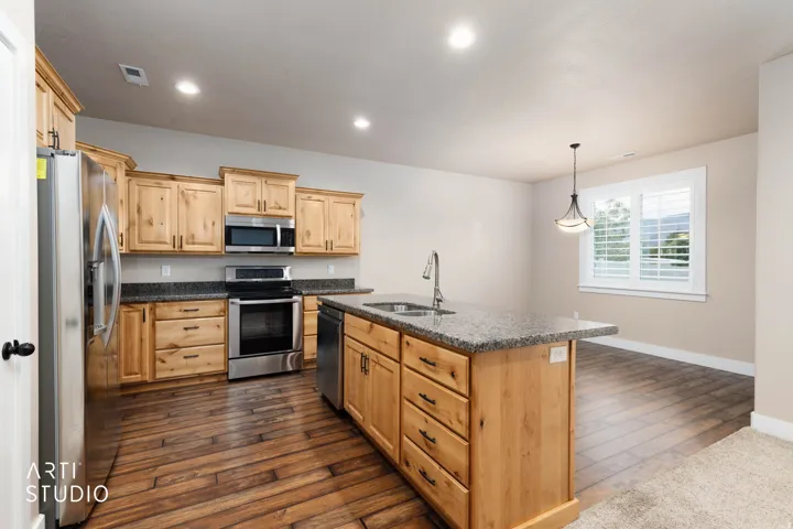 Kitchen featuring wood-finish flooring, stainless steel appliances, granite countertops, wood cabinetry, and a central island with sink
