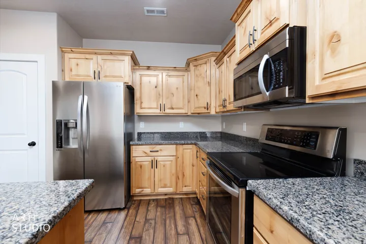 Kitchen featuring wood-finish flooring, light wood cabinetry, granite countertops, and stainless steel appliances